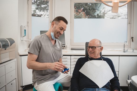 Zahnarzt und Patient lachen miteinander in einer Praxis.